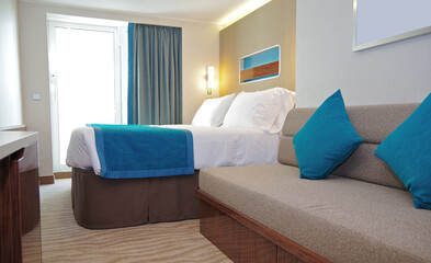 Balcony veranda bedroom stateroom cabin suite in clean modern interior design onboard luxury cruiseship cruise ship liner with pillows, duvet blanket, couch and wooden closets