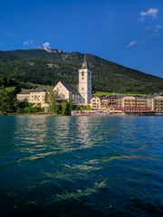 St. Wolfgang, Austria - August 16, 2019: Beautiful view from the lake to the architecture of the city of St. Wolfgang against the backdrop of the Alps. Church of St. Wolfgang is the main attraction