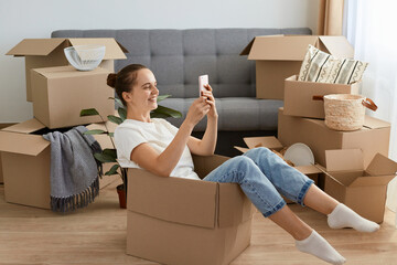 Side view of positive optimistic woman wearing white t shirt and jeans sitting in a cardboard box...
