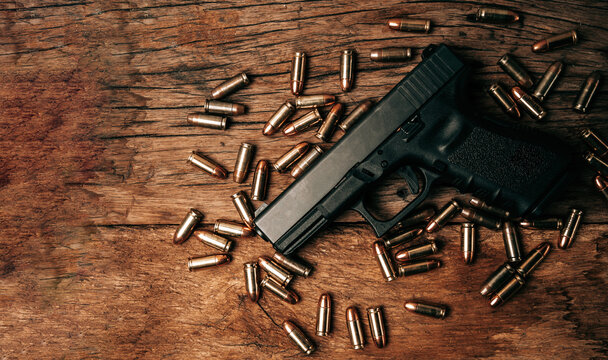Portrait of a black 9mm pistol on an old wooden floor with 9mm ammunition next to it. top view