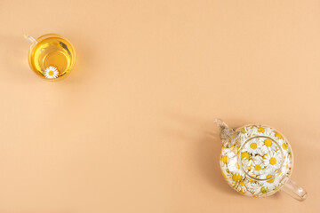 Chamomile tea. Cups of herbal tea, transparent teapot with camomile flowers on brown background. Calming drink concept. Trendy still life Copy space