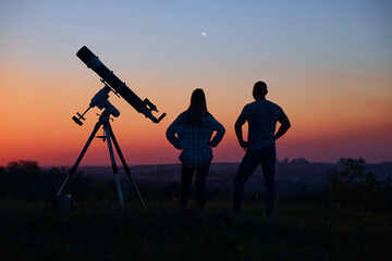 Couple stargazing together with a astronomical telescope.