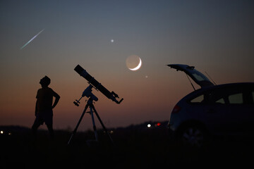 Silhouette of a man, car, telescope and countryside under the starry skies.