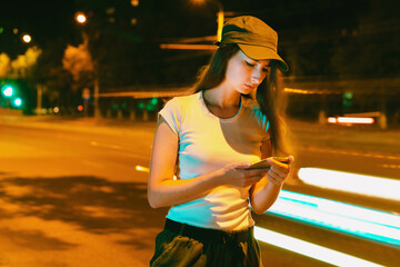Young woman waits for taxi near road in evening. Long exposure, motion blur.