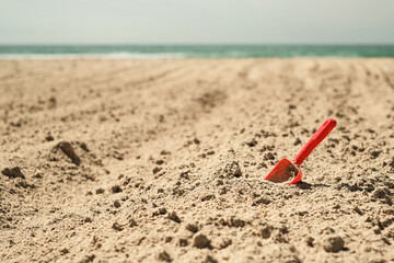 Summer children's beach toy - a red spatula on a sandy beach against the background of the sea and sky. Summer vacation banner idea