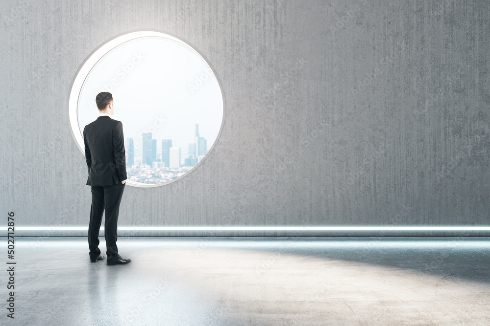 Poster back view of thoughtful young man standing in creative modern concrete interior with round window an