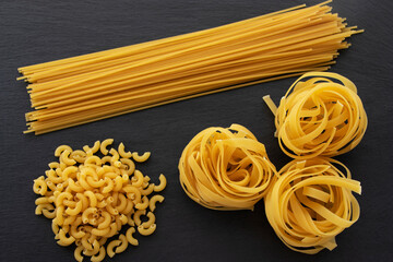 Various types of pasta lie on a black table. Italian food concept. Vegetarian.