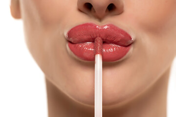 young beautiful woman apply a lip gloss on her lips on white background