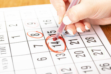 female hand marking with a red pen on a calendar circles the 14 day, deadline concept