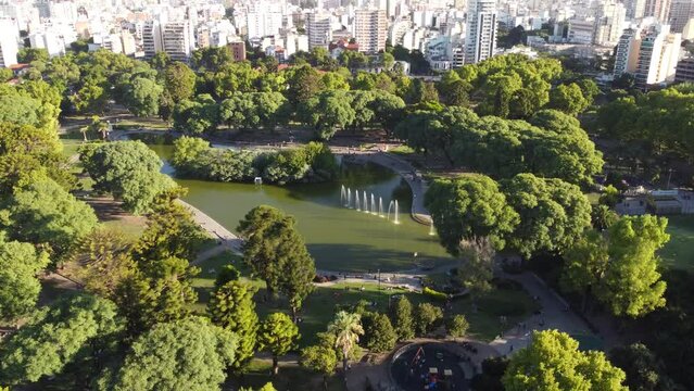Aerial orbit shot of idyllic park with lake and skyline of Buenos Aires in background