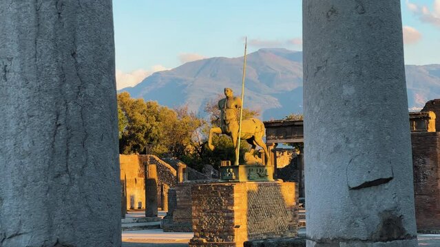 Pov forward shot of Centauro di Igor Mitoraj Statue in historic city of Pompeii lighting during golden sunset - Mountain Volcano Range in background - Italy,Europe