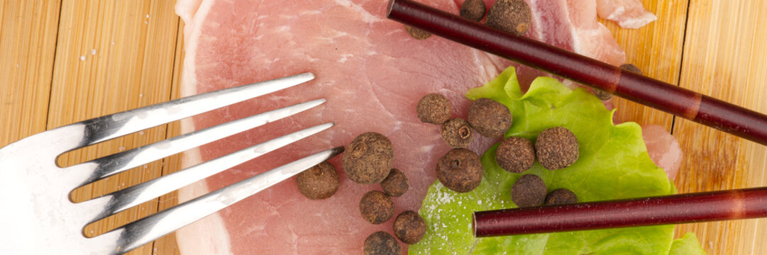 A piece of meat with a lettuce leaf and a fork with chipsticks.