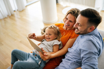 Happy young family having fun time at home. Parents with children using digital device.