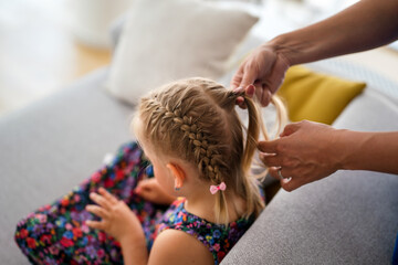 Mother is making of braids on little daughter's head. Getting ready for school.