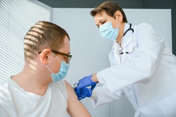 Obraz na płótnie Canvas Close up of a Doctor making a vaccination in the shoulder of patient, Flu Vaccination Injection on Arm, coronavirus, covid-19 vaccine disease preparing for human clinical trials vaccination shot.