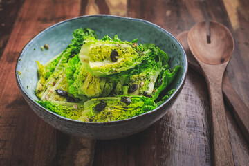 Bowl of mixed green salad with seeds on wooden background