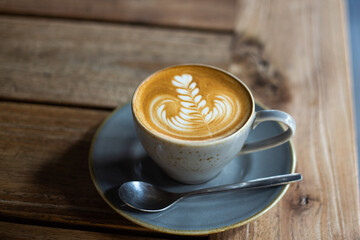 Hot coffee with latte art on wooden table at cafe