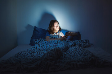 The girl lies at home in the evening on the bed with a phone in the dark. defocus