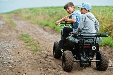 Two brothers driving four-wheller ATV quad bike. Happy children moments.