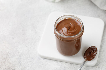 Curl of Liquid chocolate in a jar with spoon. Chocolate sauce on white board, tile background