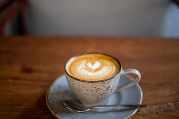 Hot cappuccino coffee cup with heart shape latte art on brown old wooden table at cafe.
