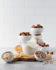 A splash of vegetable milk in a mug against the background of bowls with nuts, oatmeal and legumes. 