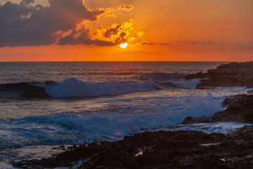 Bright beautiful stunning sea sunset, waves beating against the rocks in the rays of the setting sun