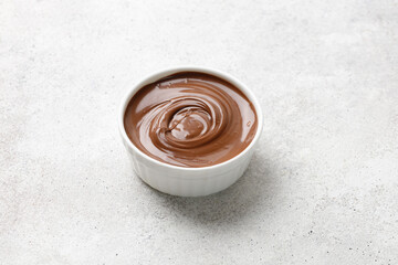 Chocolate sauce in a white saucer on grey background. Curl of Liquid chocolate. Copy space