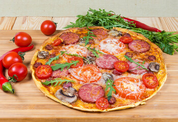 Pizza with sausages among the vegetables on wooden cutting board