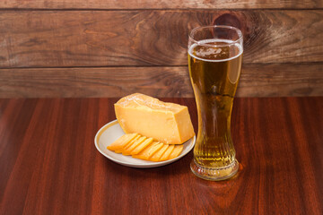 Glass of beer, hard cheese on a wooden table