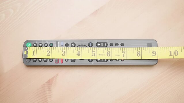Person with measuring tape measure size of 9 inch remote controller on table 4K
