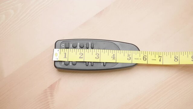 Person with measuring tape measure size of 6 inch remote controller on table 4K
