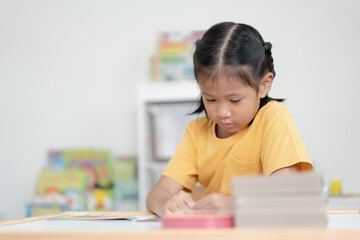 Asian schoolgirl reading book in her room. A kid enjoy reading books alone. Black hair Thai-Chinese girl concentrate reading book by her own.