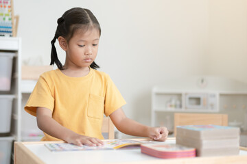 Naklejka premium Asian schoolgirl reading book in her room. A kid enjoy reading books alone. Black hair Thai-Chinese girl concentrate reading book by her own.