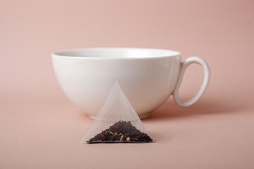 triangular tea bag and white ceramic cup on beige background