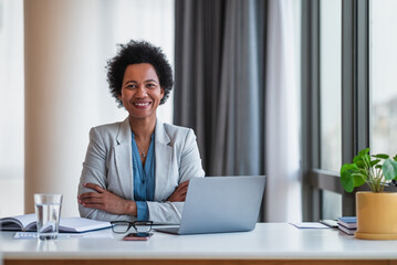 Portrait of successful happy female entrepreneur using laptop at office desk