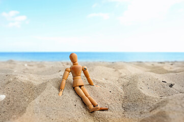 Close up of wooden mannequin sitting in the sand on the beach in front of ocean in summer with nice weather
