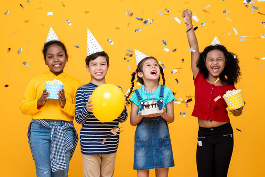 Multiethnic kids celebrating birthday party in studio yellow color background with confetti