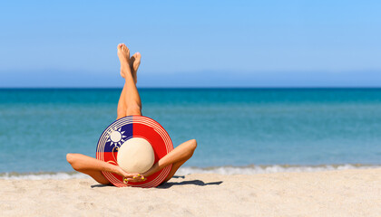 A slender tanned girl on the beach in a straw hat in the colors of the flag of Taiwan. The concept of a perfect vacation in a resort in the Taiwan. Focus on the hat.