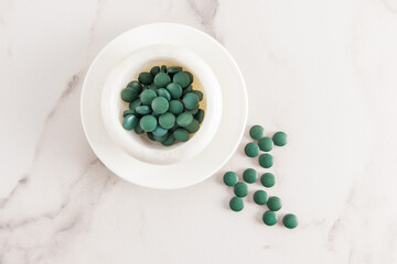 green spirulina algae tablets in a bowl on a white marble table. top view. the concept of strengthening the body. superfood.