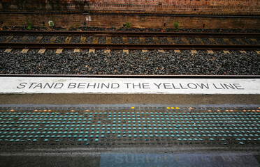 warning sign planted in black on railway platform says 