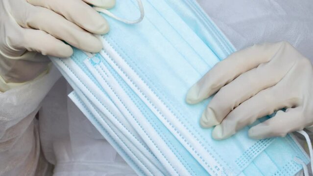 Woman doctor is holding a lot of medical protective face mask.white gloves on hands. Concept of coronavirus, air pollution, virus, flu and infectious diseases. A stack of blue color face mouth masks