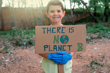 A handsome smiling young boy wearing a yellow t-shirt and blue gloves holding a cardboard sign...