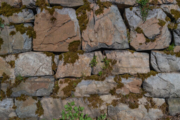 Pattern of ancient bricks and stones at old middle age fortress wall covered with moss, grass and lichen, as a background, closeup, details.