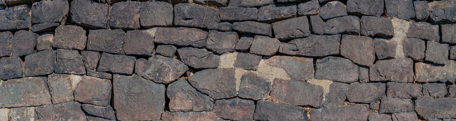 Panoramic view over a long middle age stone wall with patterns of ancient bricks and stones as a background, closeup, details.