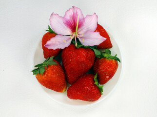 Juicy ripe fresh red strawberry and orchid tree flower isolated on white. Tasty