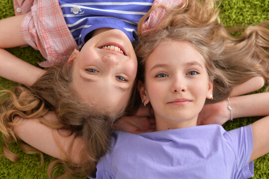 Portrait of two pretty little girls lying on green carpet and looking at camera