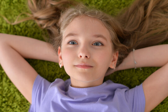 Portrait of funny smiling little girl lying on green carpet