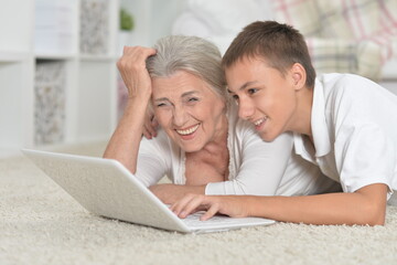 Portrait of grandmother with her grandson using laptop on carpet at home