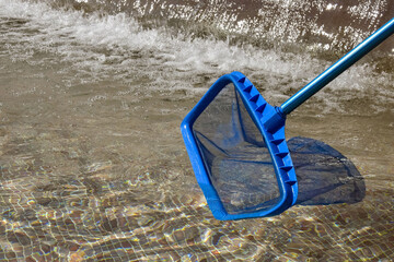 Fototapeta premium Cleaning pool, city ​​fountain from garbage with special net. Clear water with blue tint. Concept of hygiene and healthy lifestyle. Horizontal photo. Copy space. Close-up. Selective focus.